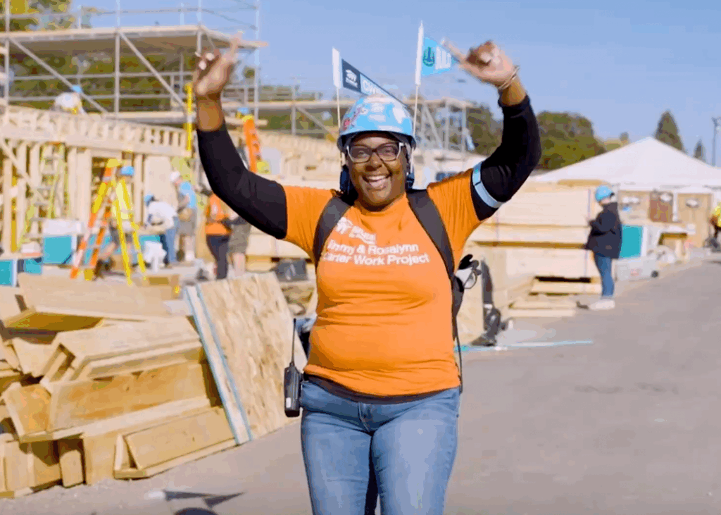Woman at a construction site, with arms raised in the air and smiling.