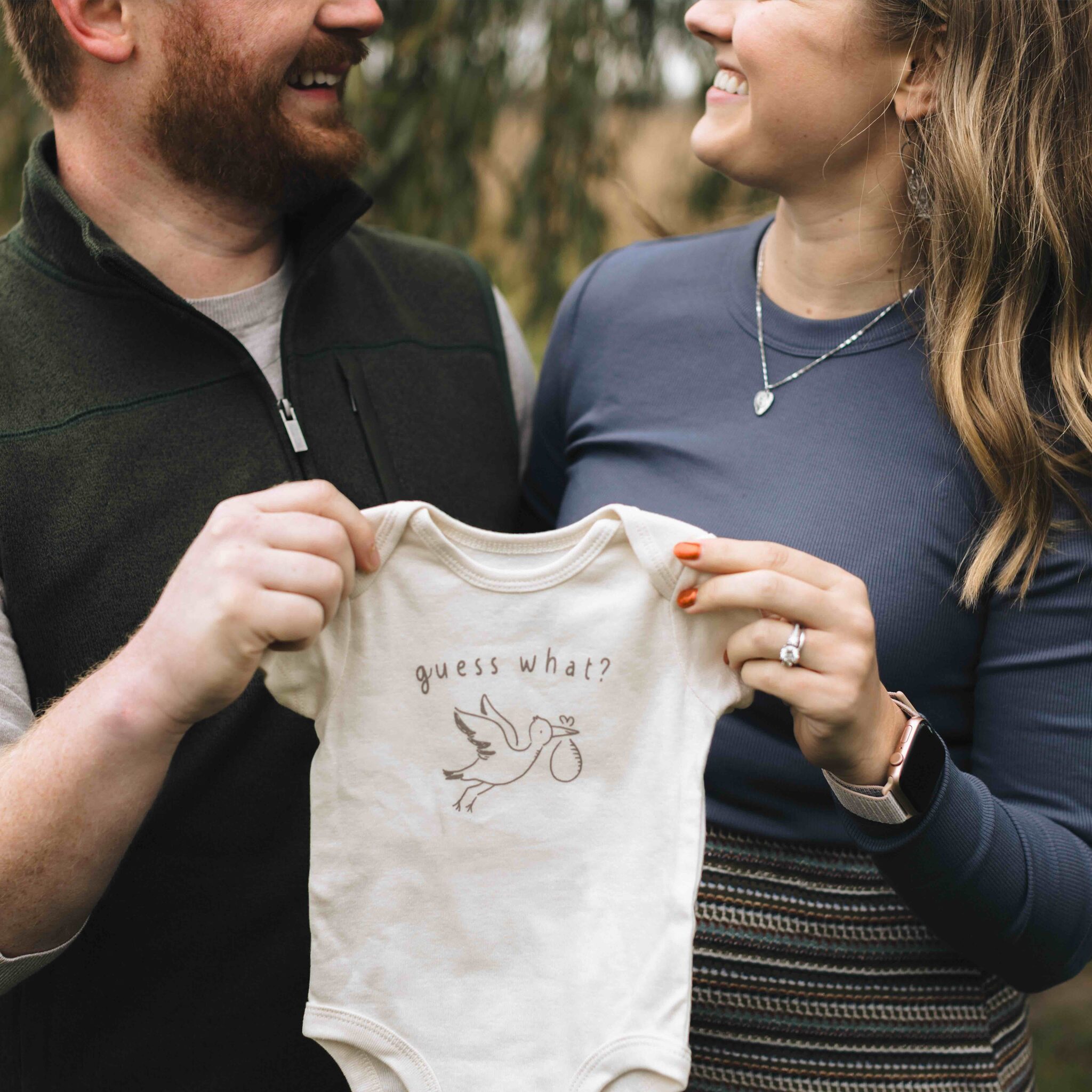 Man and woman holding a onesie that says "guess what"