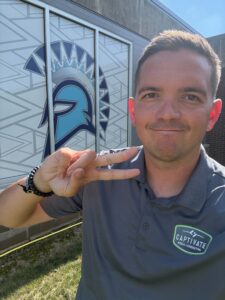 man smiling in front of a trojan logo